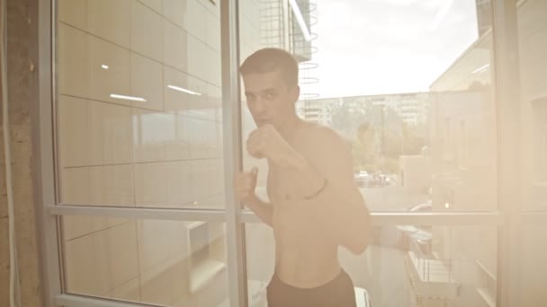 Bir atletik adam boksör pencerenin yanında duran ve kameraya boks - kamera isabet ve geriye düşer — Stok video