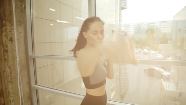 Спортивная женщина-боксер стоит у окна и боксирует перед камерой - яркий солнечный свет — стоковое видео