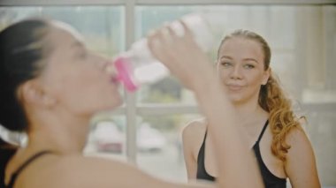 Spor salonunda duran spor kıyafetler içinde iki gülümseyen kadın - şişelerden su içmek ve konuşurken