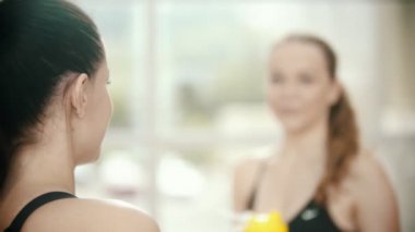 Spor salonunda duran ve şişelerden su içen iki gülümseyen kadın