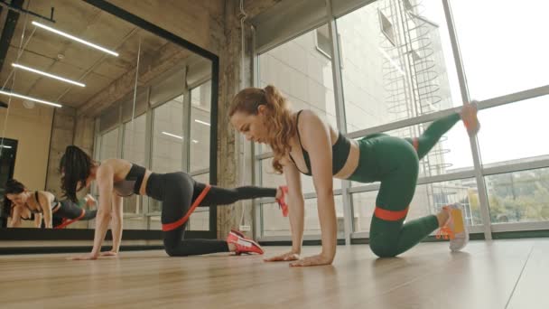 Dvě zdravé ženy si cvijí nohy pomocí roztahujících pásů mezi stehny---na kolenou a vytáhnou nohu nahoru — Stock video