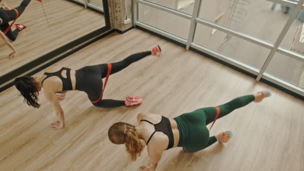 Dwie kobiety trenują nogi w studiu za pomocą paska rozciągającego między udami-stojąc na kolanach i ciągnąc nogę do góry — Wideo stockowe