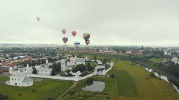 18-07-2019 Suzdal, Rusko: různé obrovské pestrobarevné vzduchové balónky létají přes vesnici a pole-různé nápisy značek na balonách — Stock video