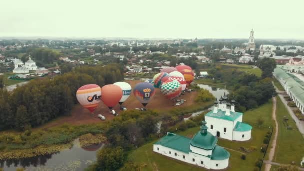 18-07-2019 Suzdal, Rusia: diferentes globos de colores están despegando sobre el campo rodeado de árboles y pueblos — Vídeos de Stock