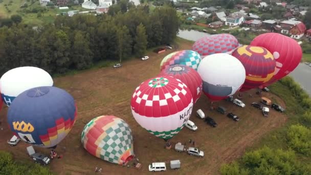 18-07-2019 Suzdal, Rússia: diferentes balões de ar coloridos sendo preparados para decolar sobre o campo - diferentes inscrições nos balões - floresta e aldeia ao redor — Vídeo de Stock