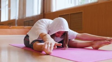 Genç kadın yoga mat üzerinde oturan ve öne eğilerek - eğilerek ve ayaklar üzerinde yere dokunarak