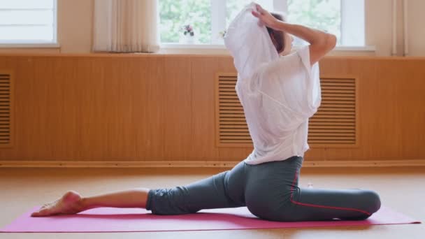 Young woman gymnast with fit butt warming up sitting on the floor and doing exercises on her legs - stretching exercises — Wideo stockowe