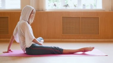 Genç kadın jimnastikçi yerde oturan ısınma ve germe egzersizleri yapıyor