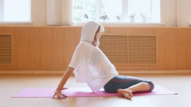 Genç ince kadın dans stüdyosunda yoga minderi üzerinde oturan ısınma