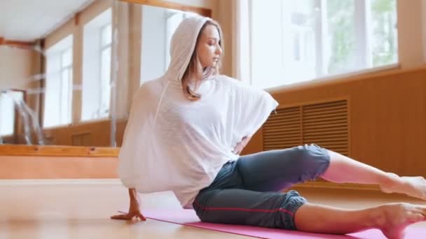 Junge schlanke Frau wärmt sich auf, sitzt auf der Yogamatte und macht Beinübungen - ergreift den Fuß und zieht das Bein — Stockvideo