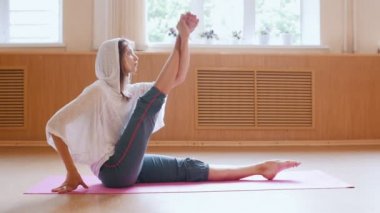 Genç ince kadın yoga mat üzerinde oturan ısınma - ayak kapma ve germe için bacak egzersizleri yapıyor