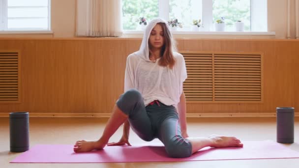 Jonge slanke vrouw zittend op de yoga mat met haar knieën samen en trekken haar handen omhoog — Stockvideo