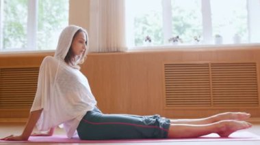 Genç ince kadın jimnastikçi yerde oturan ısınma ve bacaklarında hafif egzersizler yapıyor - germe egzersizleri