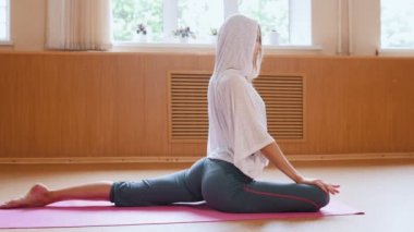 Genç ince kadın jimnastikçi yerde oturan ısınma ve bacaklarında egzersizler yapıyor - germe egzersizleri