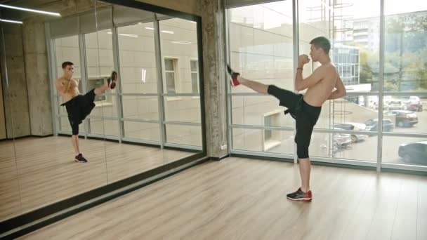 Un hombre atlético de pie en el estudio y entrenando su boxeo frente al espejo — Vídeo de stock