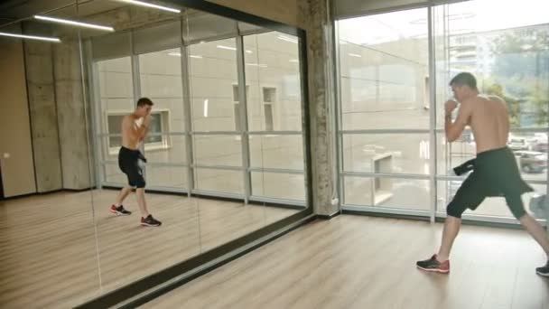 Un hombre sin camisa atlético parado en el estudio y entrenando su boxeo frente al espejo — Vídeo de stock