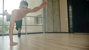 Stüdyoda çıplak gövde eğitimi ile atletik bir adam - itme up yapıyor ve bir yandan ayakta ve ileri başka bir el çekerek - dayanıklılık eğitimi