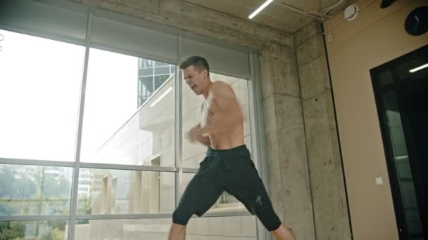 Un boxeur d'homme athlétique debout près de la fenêtre et effectuant un combat avec une ombre - entraînement d'endurance avec un effort — Video