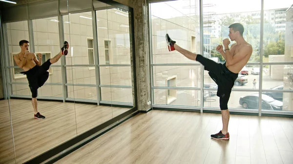 Un uomo atletico senza maglietta in piedi in posa combattimento in studio - calci - allenamento davanti allo specchio — Foto Stock