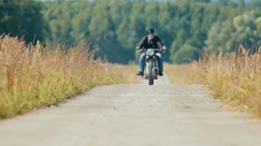 Tozlu çavdar tarla yolunda motosiklete binen bir adam motosikletçi