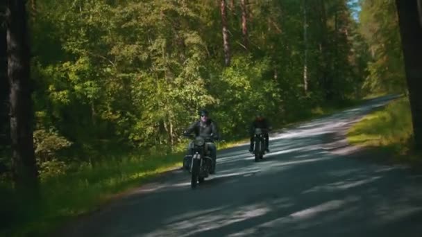 Dois homens brutais motociclistas no capacete montando uma moto na floresta — Vídeo de Stock