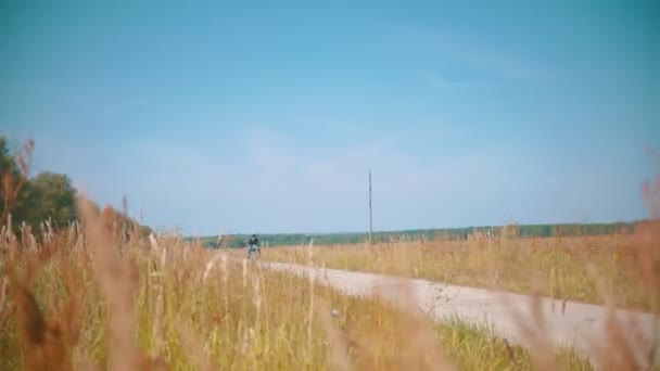 A man motorcyclist riding motorbike on the dusty country road above the rye field — Stock Video