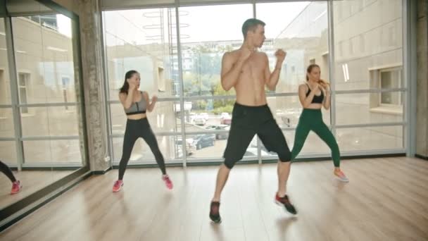 Entrenamiento de fitness en el estudio - dos mujeres jóvenes entrenando con su entrenador - saltando en el lugar y golpeando el aire — Vídeo de stock