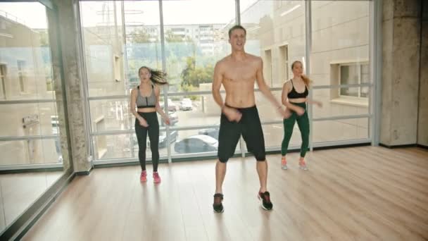 Fitness výcvik ve studiu-dvě mladé ženy trénující s trenérem-skákání na spotové opakované cvičení-jedna žena se unaví a přestane trénovat — Stock video