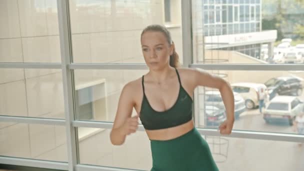 Una boxeadora atlética de pie junto a la ventana y el boxeo - entrenando su ponche — Vídeos de Stock