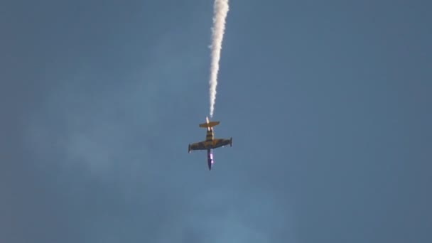 Sebuah pesawat reaktif biru dan kuning terbang turun di langit dan melakukan pertunjukan dengan melepaskan asap berputar di sekitar dirinya sendiri — Stok Video