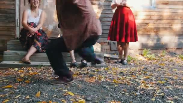 Женщина, играющая на балалайке, и мужчина, танцующий русский фольклор возле загородного дома - яркий солнечный свет — стоковое видео