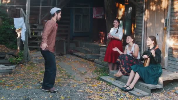 Women sitting on the stairs and one of them playing balalaika - a man dancing folk dances — Stock Video