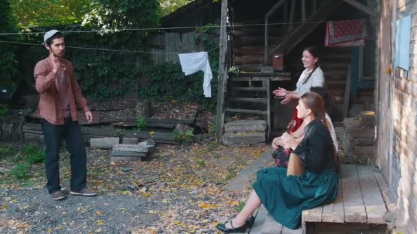 Glückliche Frauen sitzen auf der Treppe und eine von ihnen spielt Balalaika - ein Mann tanzt Volkstänze — Stockvideo