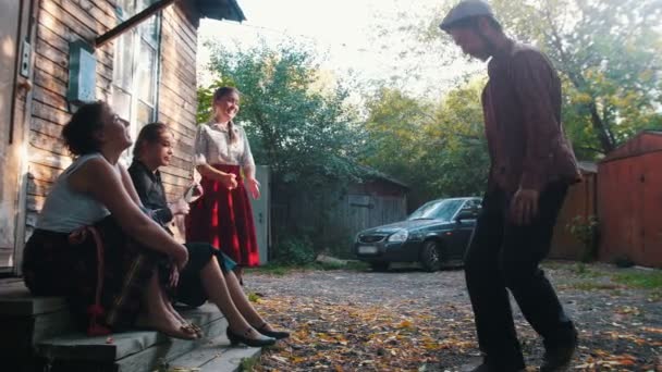 Women sitting on the stairs near the country house and one of them playing balalaika - a man dancing folk dances — Stock Video