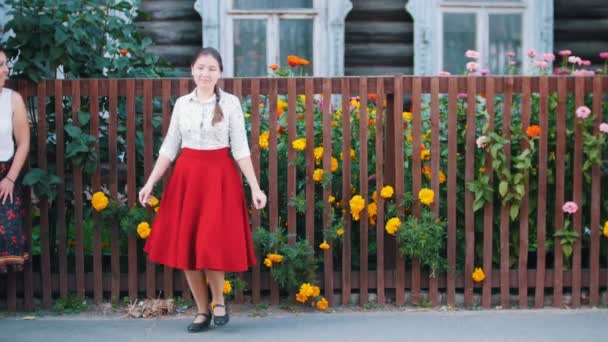 A young woman in long red skirt dancing by the fence on the street — Stock Video