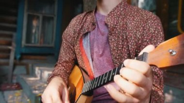 Açık havada balalaika oynayan sakallı bir adam - kır evinin yakınındaki merdivenlerde oturuyor