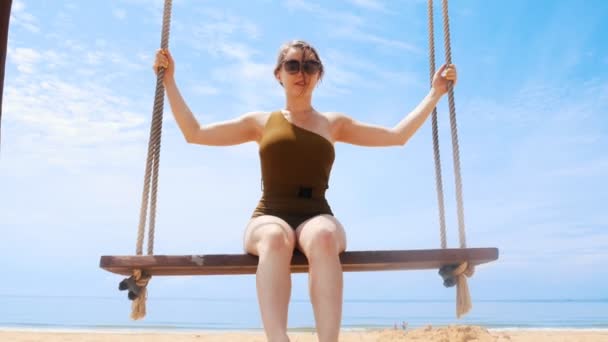 Молодая красивая женщина качается на качелях на пляже — стоковое видео