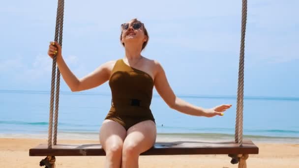 해변에서 그네에 스윙 녹색 수영복에 젊은 부주의 한 여자 — 비디오