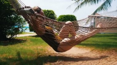 Tropik bitkilerin etrafında hamak yalan mayo genç bir güzel kadın ve onun tatil keyfini çıkarın