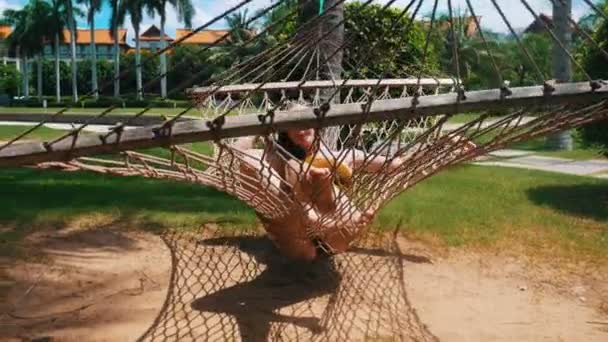 Een jonge mooie vrouw liggend in de hangmat rond tropische planten en het hebben van een rust — Stockvideo