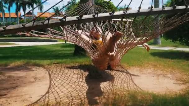 Mladá žena ležící v houpací síti kolem tropických rostlin a odpočívej — Stock video