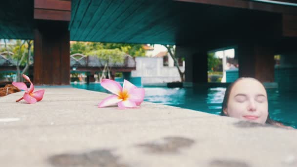 Een jonge vrouw komt uit het zwembad en pakt een bloem op en zet hem in haar haar — Stockvideo