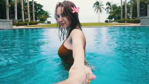 Молодая женщина с мокрыми волосами ведет своего парня в бассейн за руку — стоковое видео