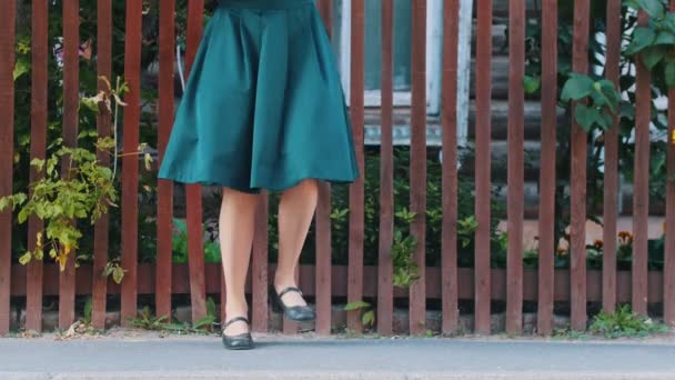 Eine junge schlanke Frau im smaragdgrünen Rock tanzt in schwarzen Schuhen am Zaun — Stockvideo