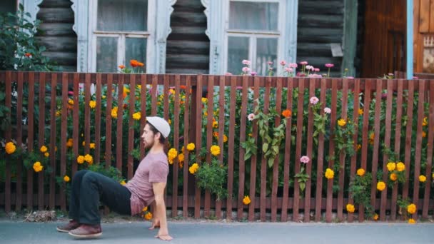 Un hombre bailando danza popular rusa junto a la valla con flores en el pueblo — Vídeos de Stock