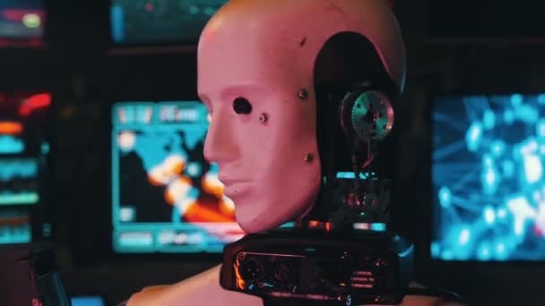 Robot futurista sentado junto a los monitores con la cabeza girando — Vídeo de stock