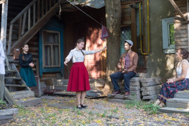 Kırmızı etekli bir kadın kır evinin yakınında müzik eşliğinde dans ediyor - merdivenlerde balalaika çalan bir adam