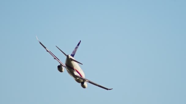 Un avión de pasajeros con rayas de color rojo y azul volando en el cielo despejado — Vídeos de Stock