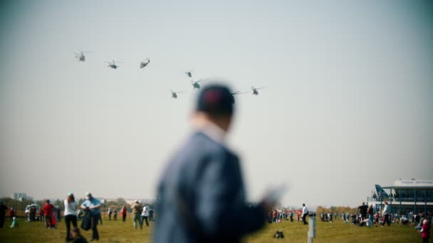 Gente mirando helicópteros volando en el cielo gris — Vídeo de stock