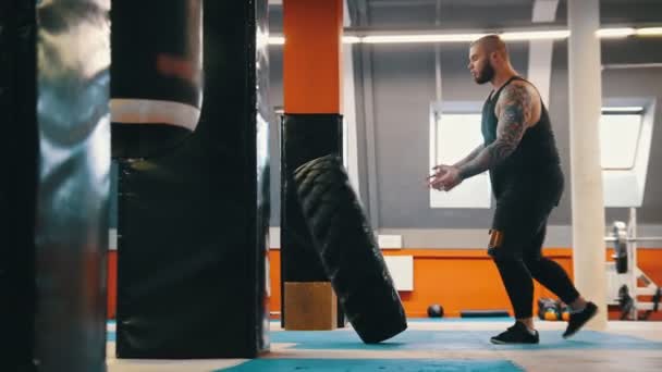 Un culturista hombre voltea un neumático en el suelo una y otra vez en el gimnasio — Vídeos de Stock